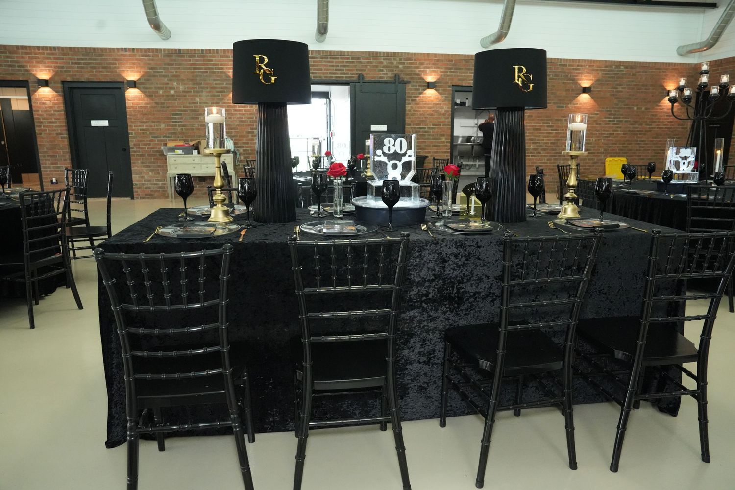 Elegant black banquet table with velvet chairs, candelabras, and gold-accented lamps set for an 80th birthday celebration.