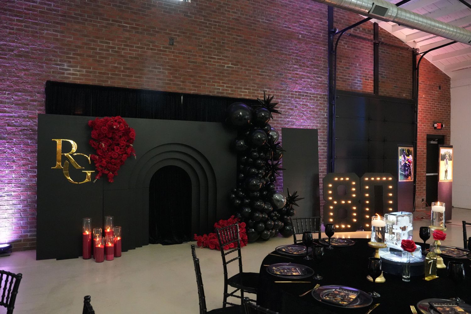 Sophisticated event venue with black arch backdrop, RG monogram, red floral decor, and illuminated 80 number display.