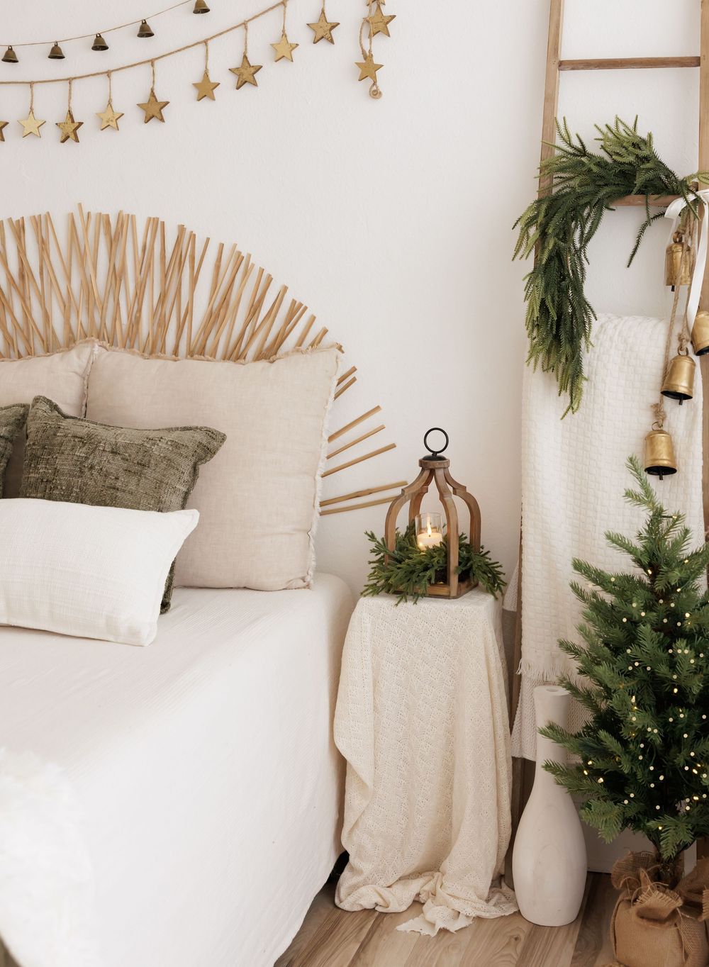 Boho Christmas bedroom with rattan headboard, green pillows, mini tree, lantern, ladder with bells and garland.