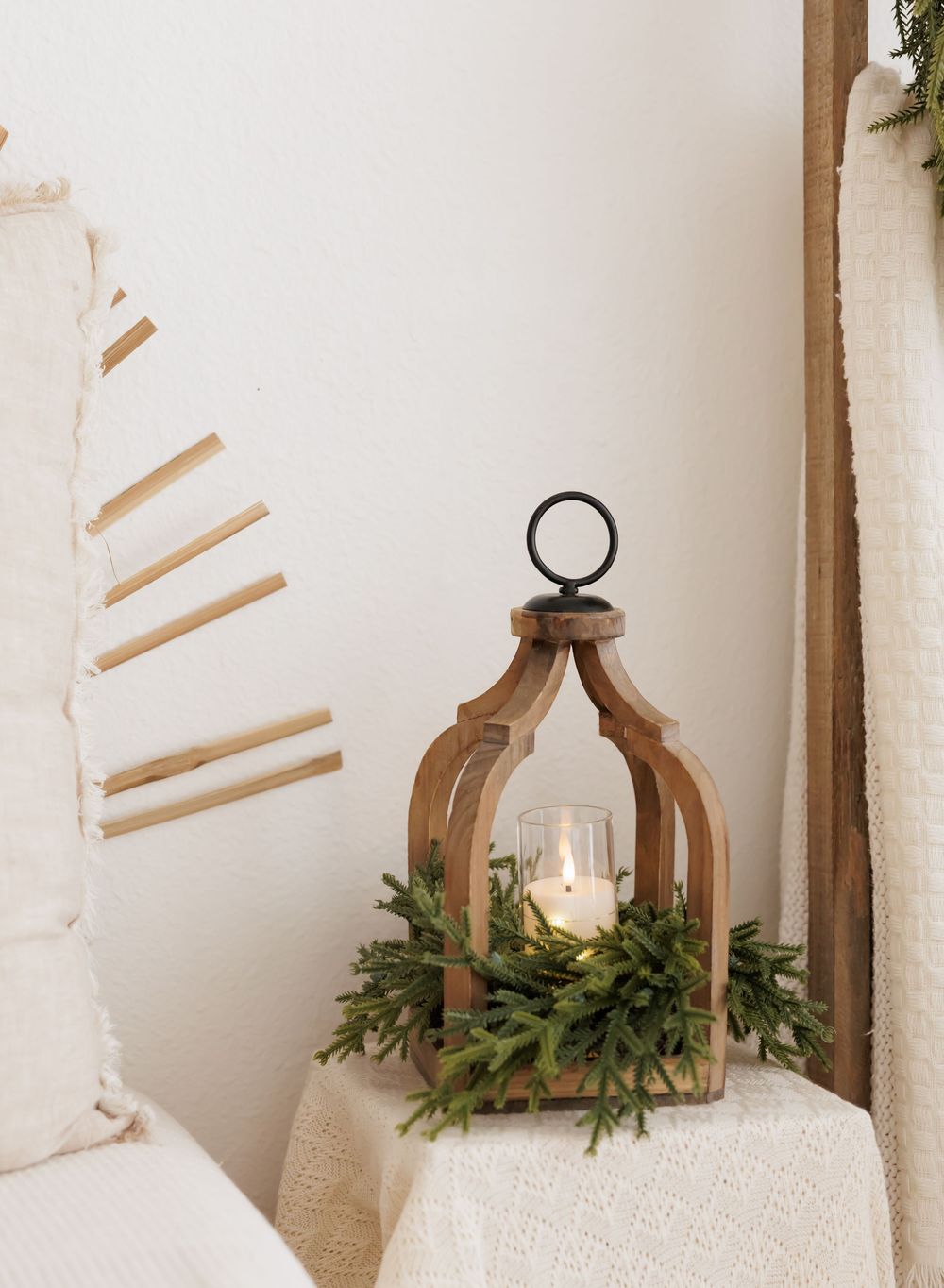 Wooden arch lantern with candle and greenery wreath on white draped table, beside minimalist wall decor.