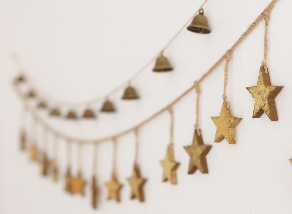 Gold star and bell garland hanging on a white wall, perfect for festive holiday decor.
