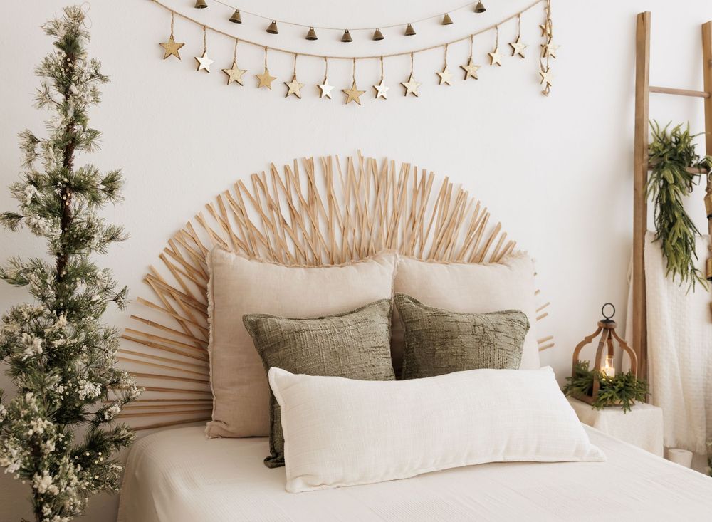 Bohemian bedroom with woven sunburst headboard, green pillows, Christmas tree, and gold star garland.