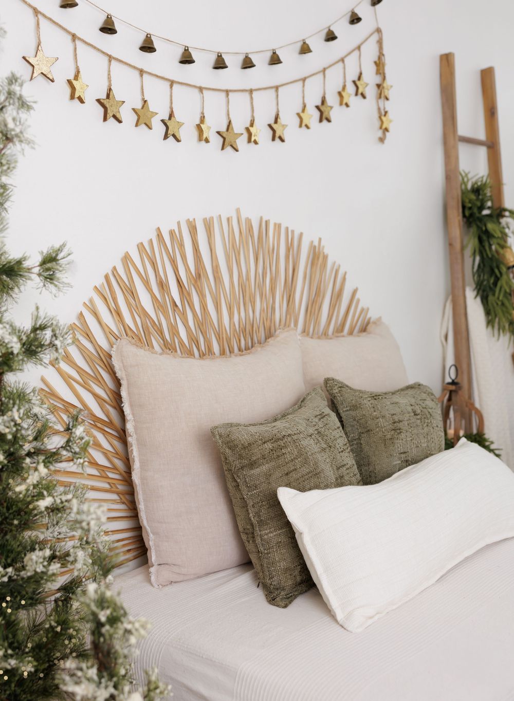 Boho rattan sunburst headboard with neutral and green pillows, gold star garland, and festive greenery for holiday decor.