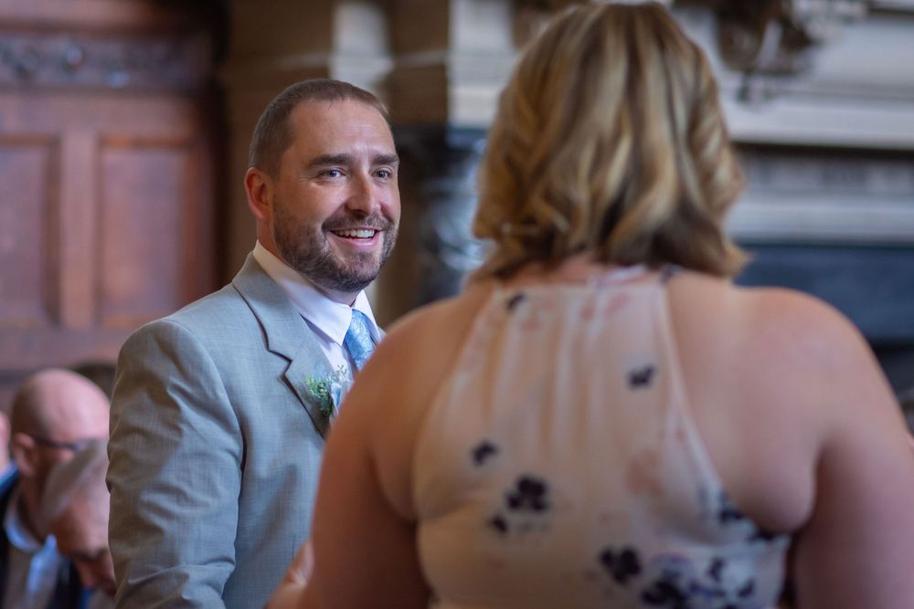 A smiling groom in a gray suit chats with a woman in a floral dress at a wedding reception.