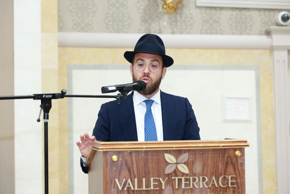 Man in suit and black hat speaking at Valley Terrace podium with microphone.