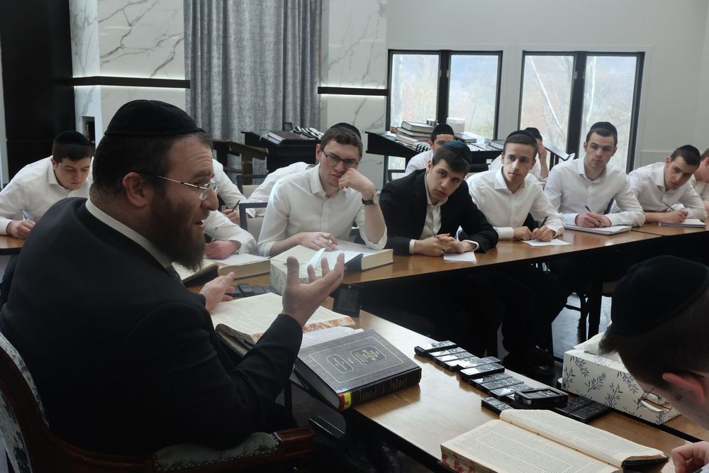 Rabbi teaching Jewish students in a yeshiva classroom, engaged in Torah study discussion.