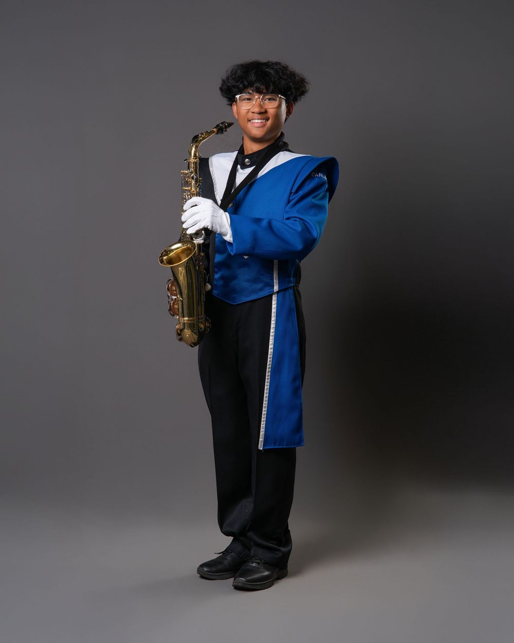 Young marching band member in blue uniform holding a saxophone, smiling and posing for a portrait photo.