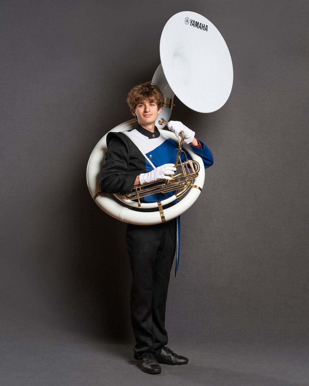 Young musician in marching band uniform holding a Yamaha sousaphone, posing against a gray background.