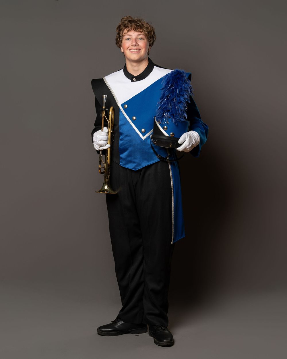 Young male marching band member in blue and white uniform holding a brass instrument, wearing white gloves.