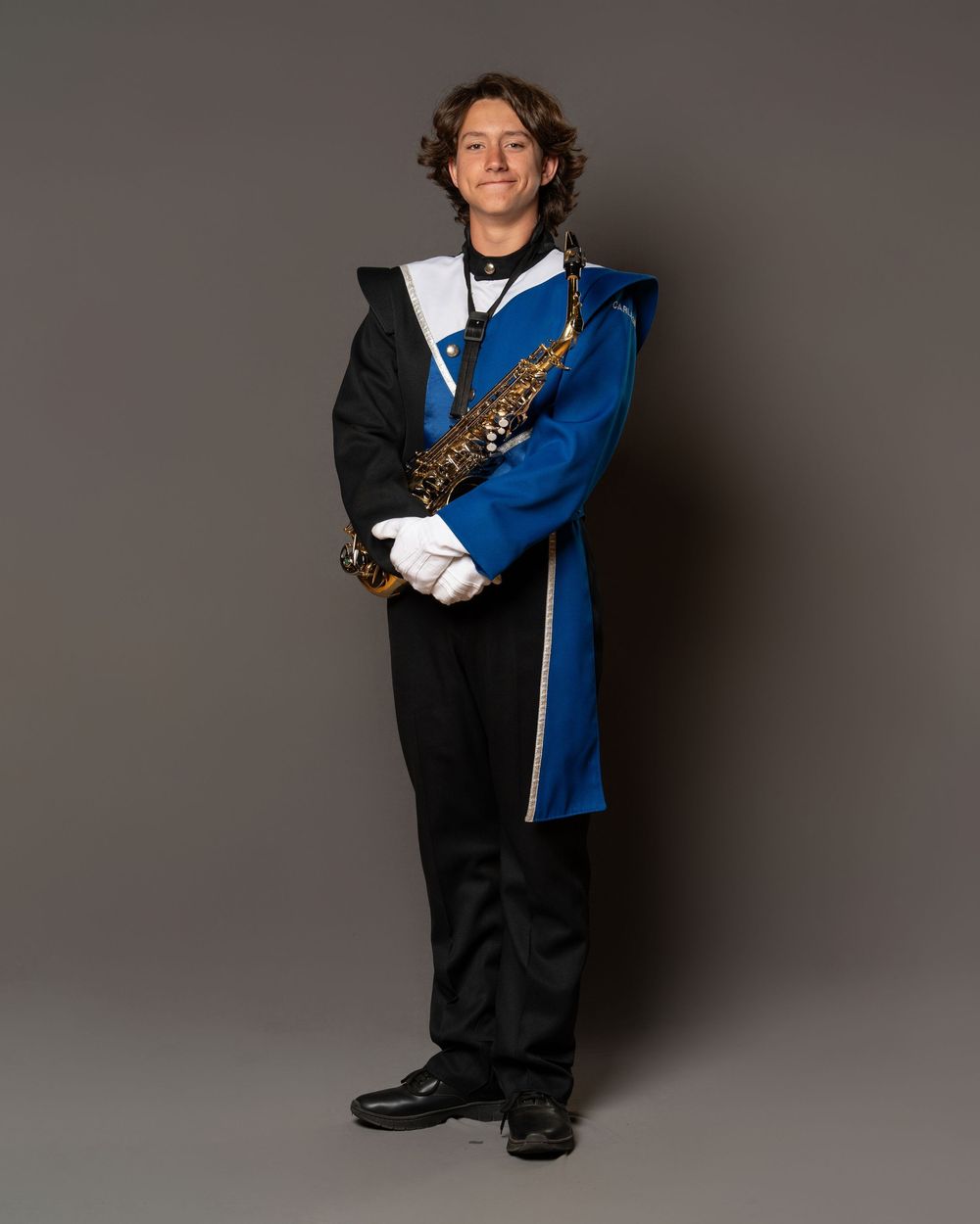 Student in blue and black marching band uniform holding a saxophone, wearing white gloves, posing for portrait.