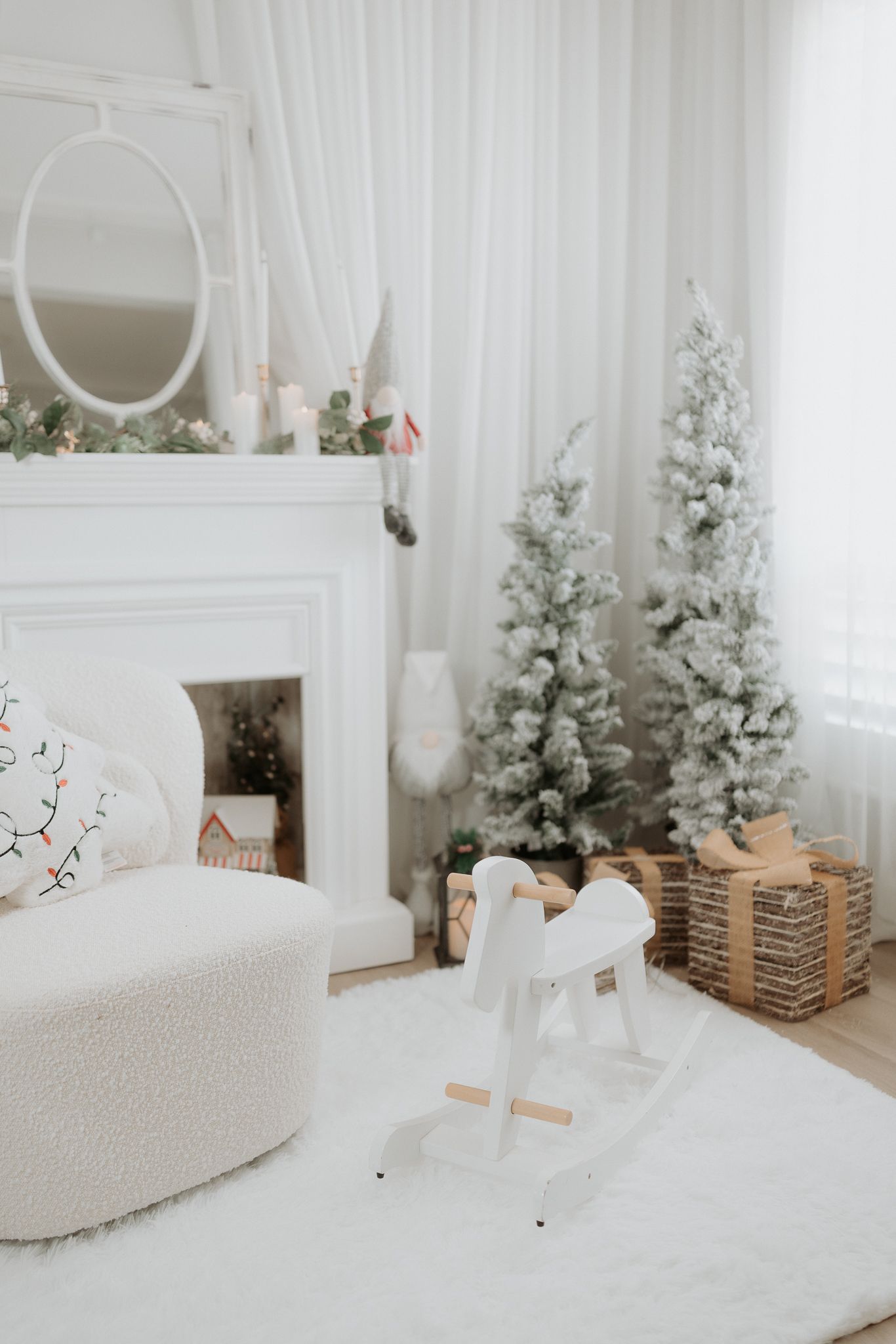 White Christmas living room with flocked trees, gifts, rocking horse, and decorated fireplace mantel.