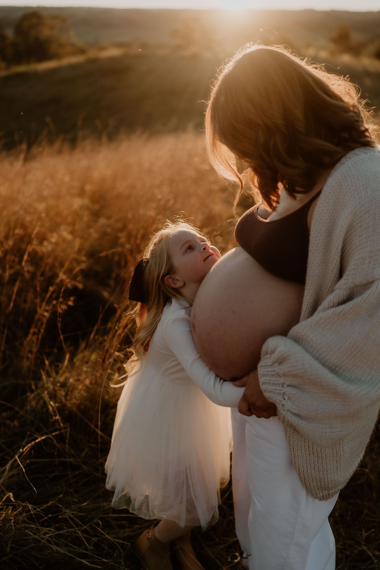 Young girl cuddles her pregnant mother during newborn photography session in Picton NSW