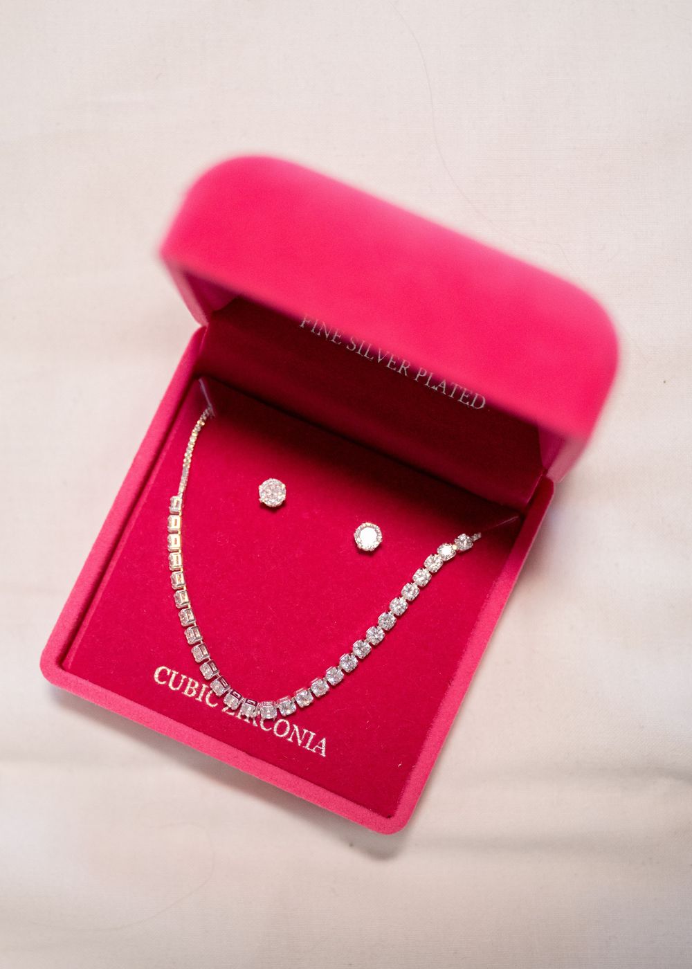 Silver cubic zirconia tennis necklace and stud earrings set displayed in a pink velvet jewelry box.