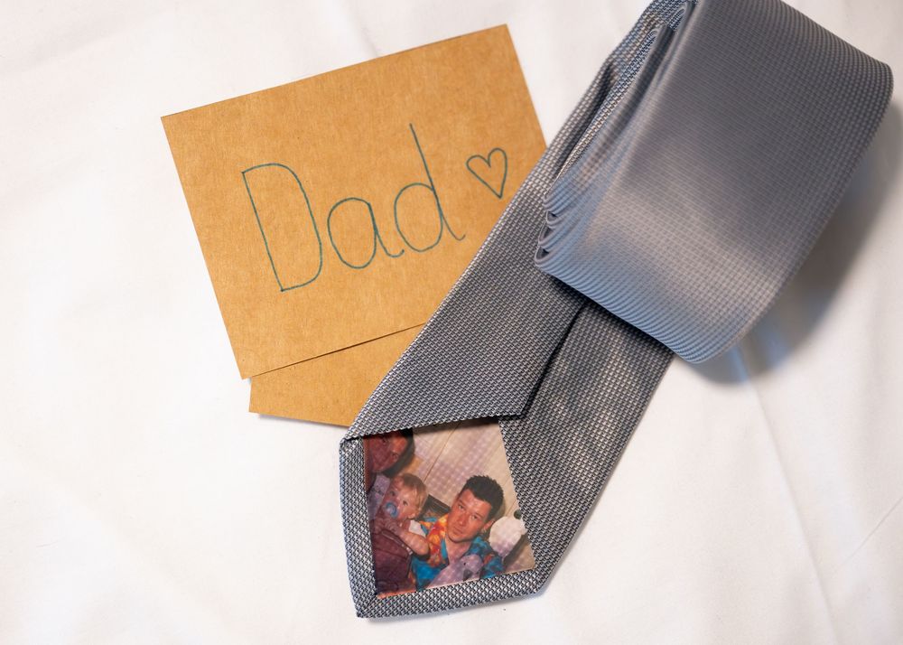 A gray necktie with a family photo print beside a handwritten Dad card on white background.
