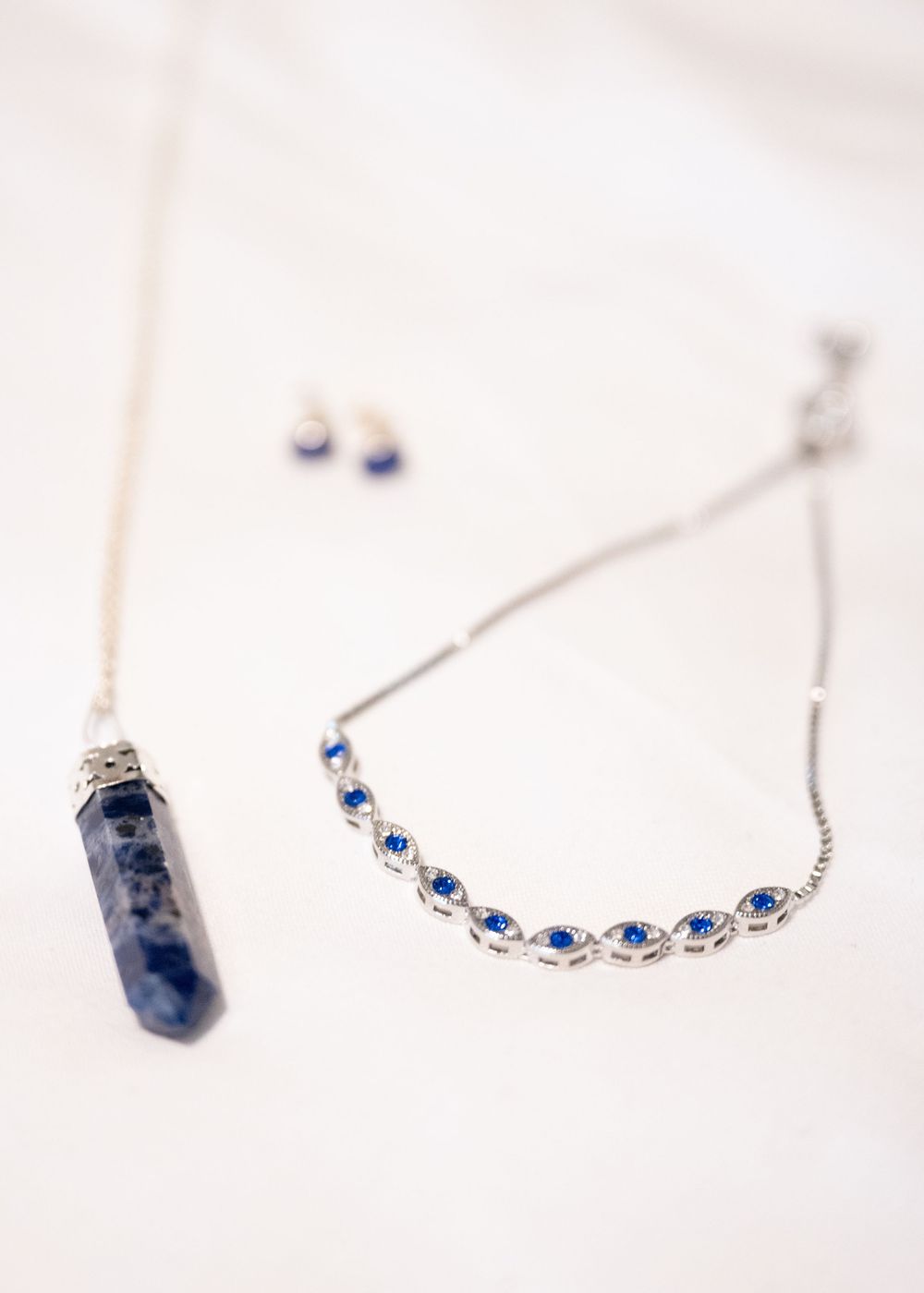 Blue gemstone crystal pendant and sapphire rhinestone necklace with matching earrings on white surface.