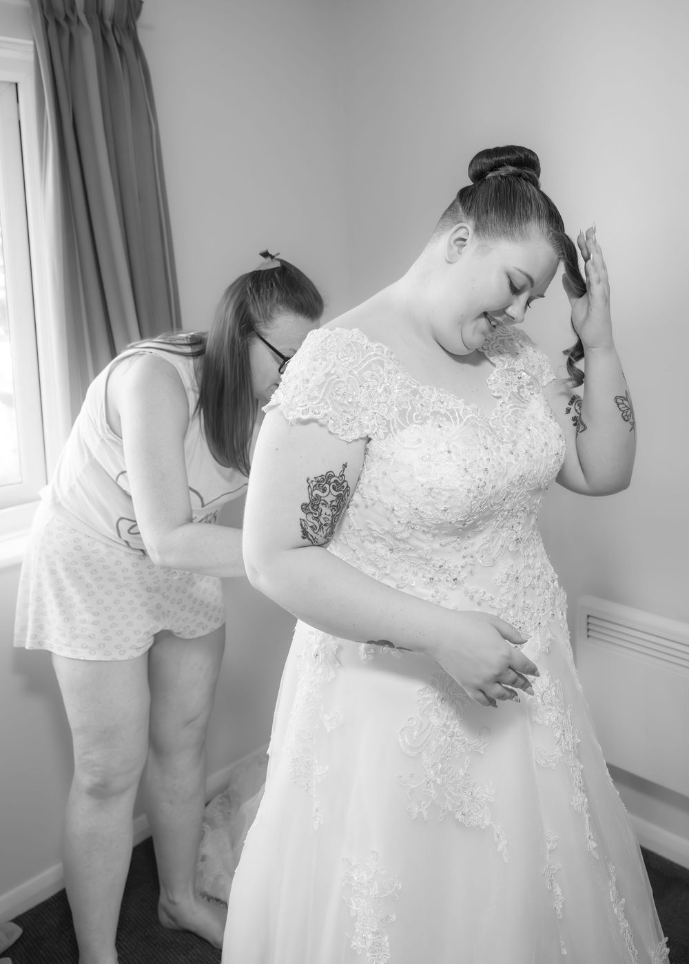 Bride in lace wedding gown being helped by bridesmaid in black and white getting ready photo.