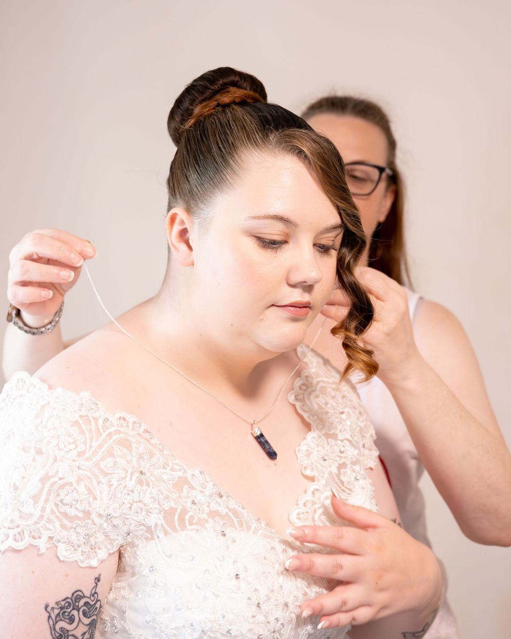 A bride in a lace wedding dress gets her hair styled by a beautician before her wedding ceremony.