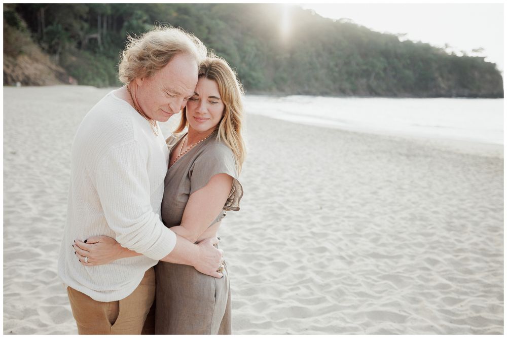 One & Only Mandarina Couple Photographer capturing an engaged couple embracing on the beach at sunset with lush coastal hills behind them.