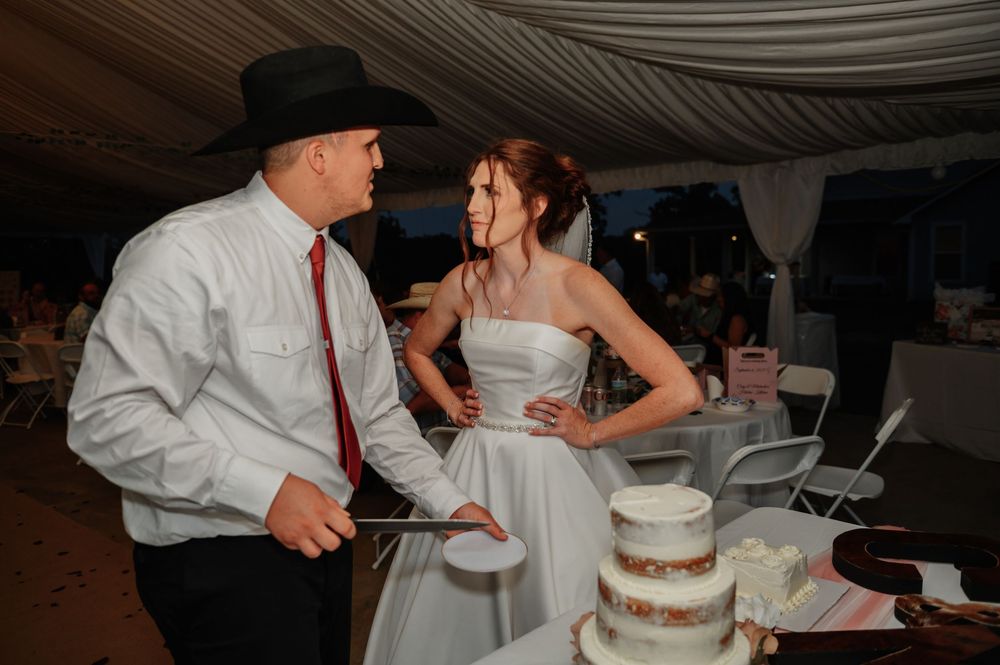 Bride and groom cutting their wedding cake at a reception, groom wearing cowboy hat and red tie.