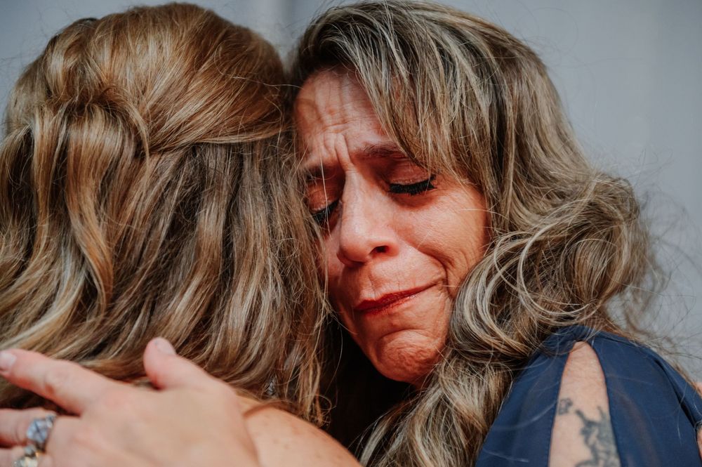 Two women with highlighted hair share an emotional hug, one visibly crying, in a heartfelt embrace.