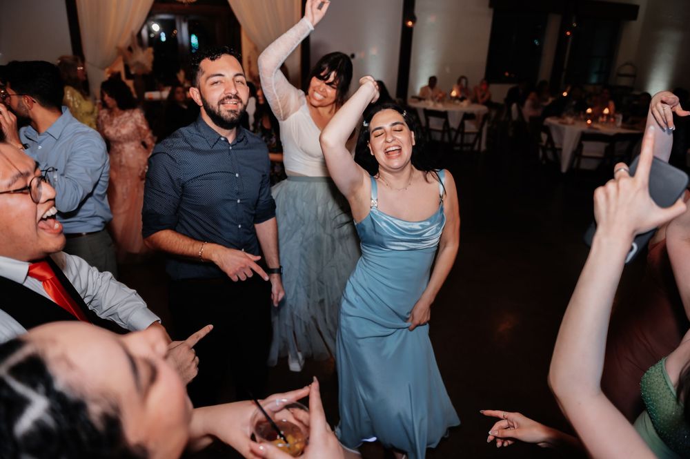 Wedding guests dancing joyfully at a reception, woman in blue dress and man in blue shirt celebrating on the dance floor.