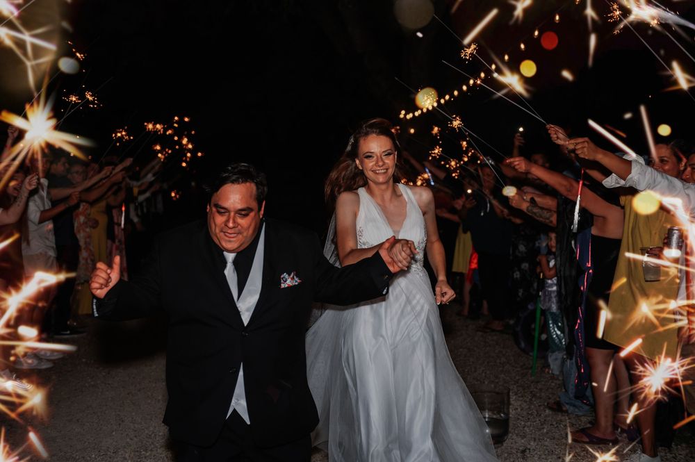 Bride and groom walk through sparkler tunnel at night wedding celebration.