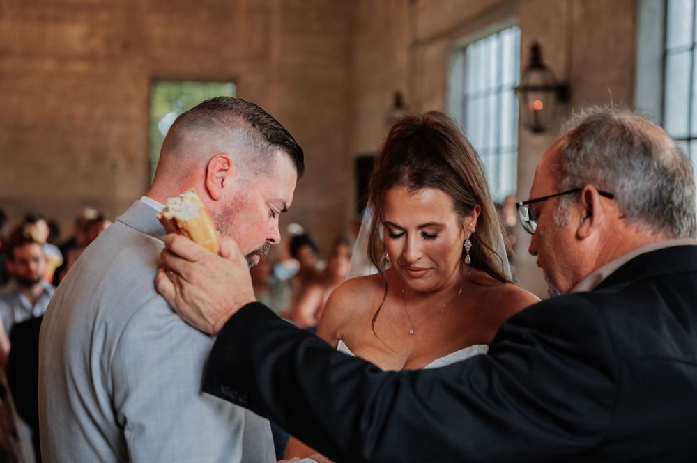 Emotional wedding ceremony moment with bride and groom sharing a tender exchange with officiant indoors.