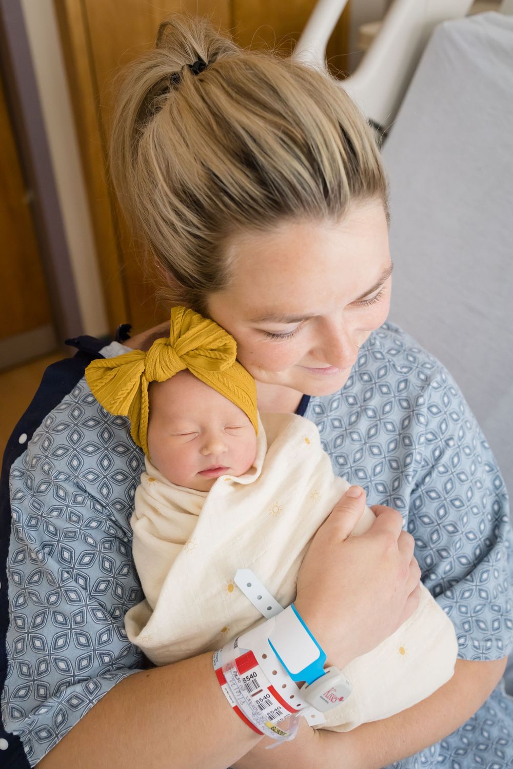 New mother in hospital gown lovingly holds sleeping newborn. Images at Fort Sanders Medical Center in Knoxville, TN by Nina Thomas Photograp