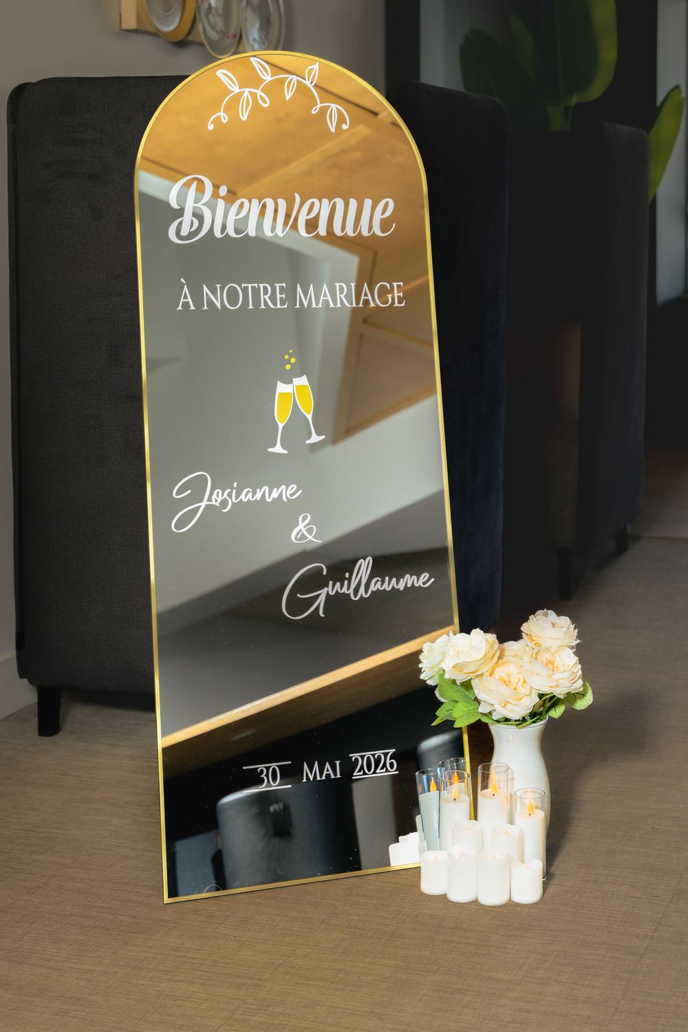 Miroir de bienvenue de mariage avec lettrage blanc, vase de fleurs roses et bougies allumées au sol.