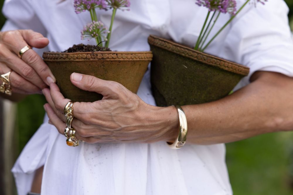 Close-up of a woman in white holding terracotta pots, wearing gold rings and a bracelet.