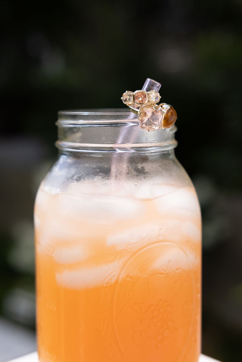 A mason jar filled with icy peach-colored lemonade, garnished with a decorative gold charm on a straw.