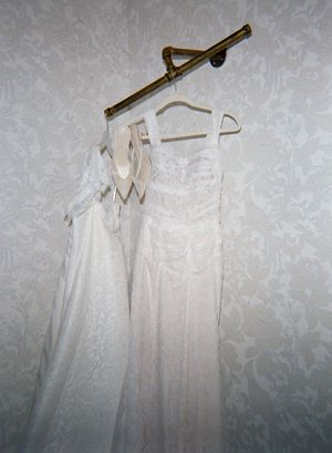 Several white bridesmaid dresses hanging on wooden hangers against a textured grey wall.