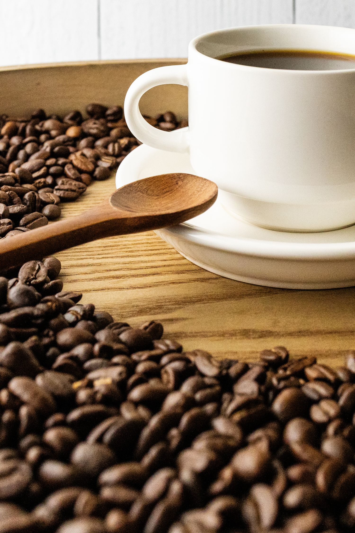 Cup of black coffee on a wooden serving tray with beans in the foreground and a wooden styling spoon.