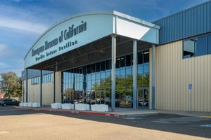 Exterior of the Aerospace Museum of California Pacific Visitor Pavilion with a curved glass-front entrance under a clear blue sky.