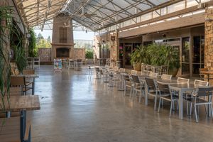 Spacious covered patio dining area with rows of metal tables and chairs, a stone fireplace, potted plants, and a polished concrete floor.