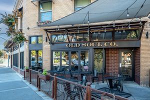 Old Soul Co. cafe exterior with brick facade, large windows, string lights, and a fenced outdoor patio with black bistro tables and chairs.