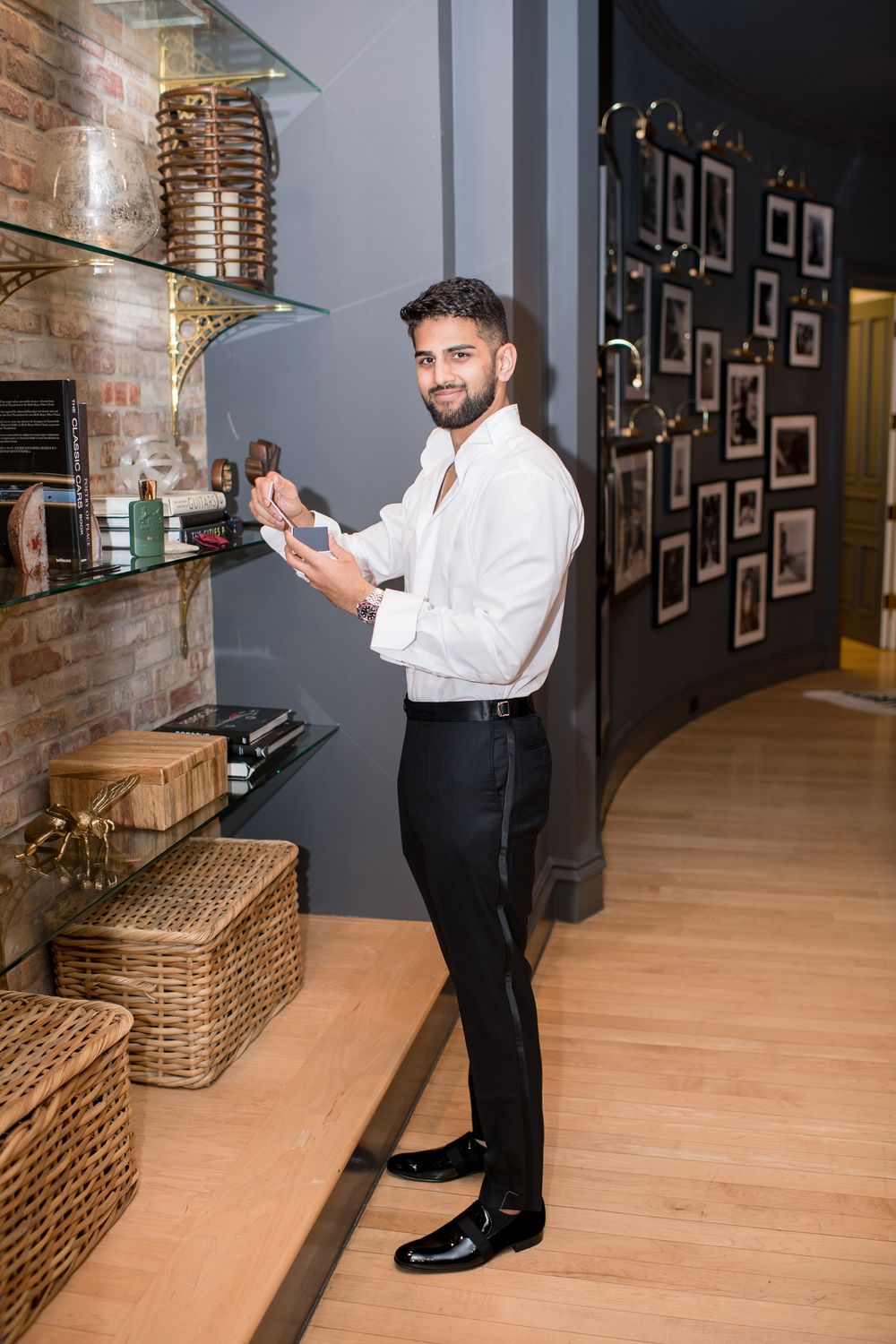 Elegant man in white dress shirt and black trousers standing by a decorative shelf in a stylish room.