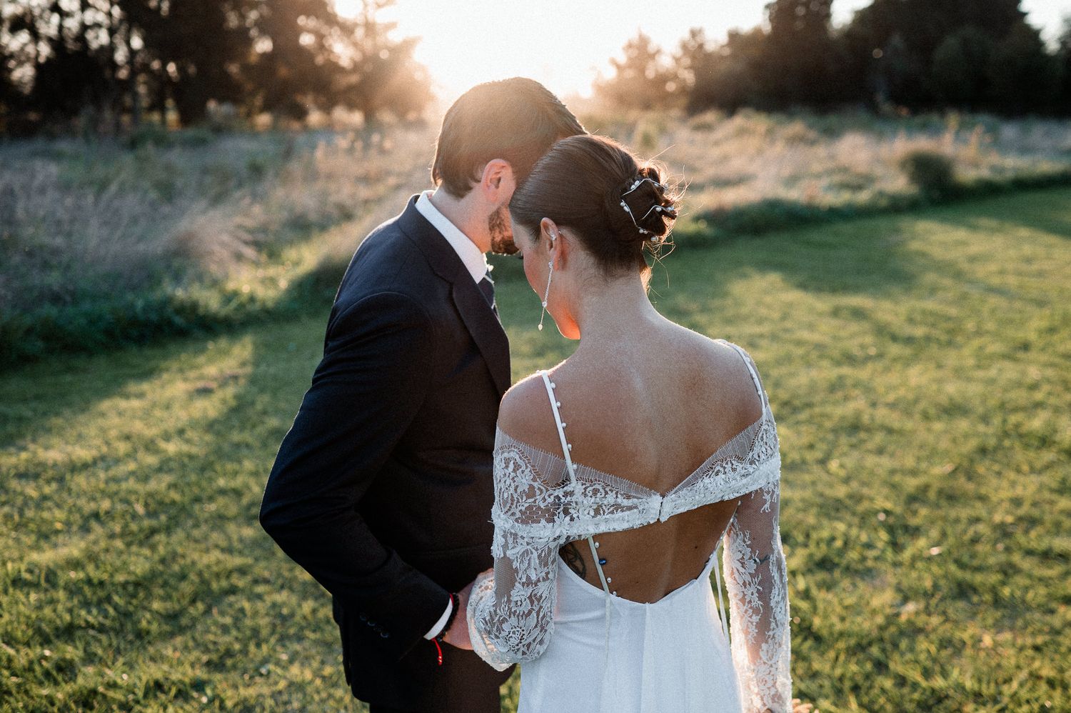 Intimate wedding portrait of newlyweds embracing on manicured lawn during golden hour.