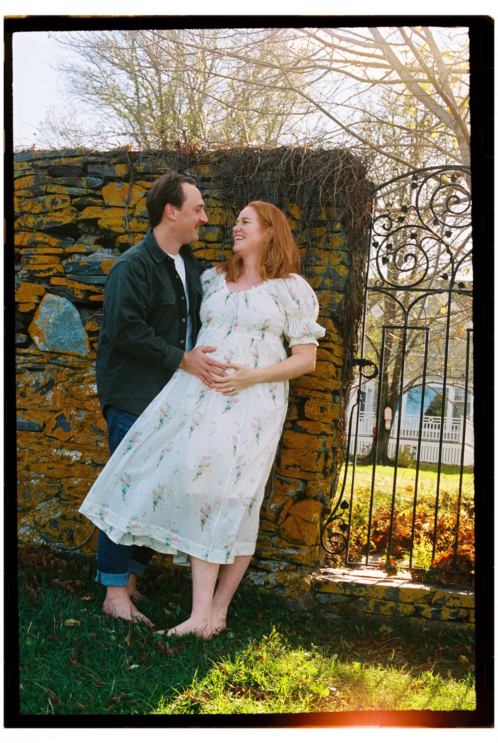 Couple embraces by a stone wall in the afternoon sunshine during an early November maternity photoshoot at Willard beach in South Portland.