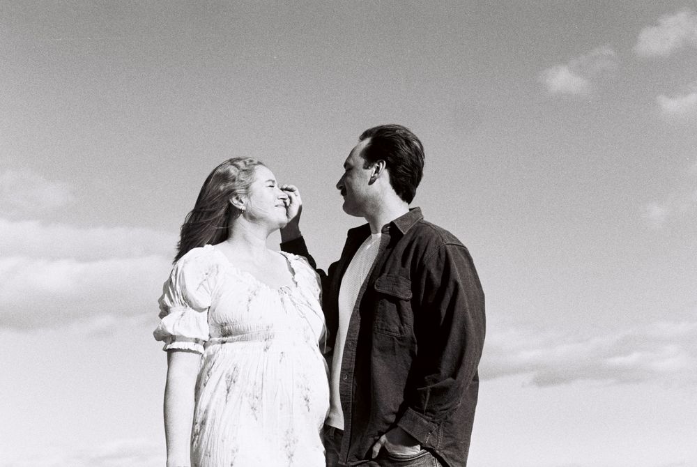 Black and white photo of couple set against the sky while he caresses her hair during a sunny maternity photoshoot at Willard Beach in Maine