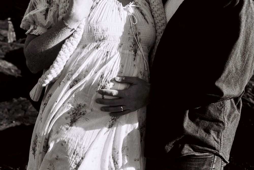 Detail photo of husband lovingly touching his wife's pregnant belly during a photoshoot on black and white 35mm film in South Portland.