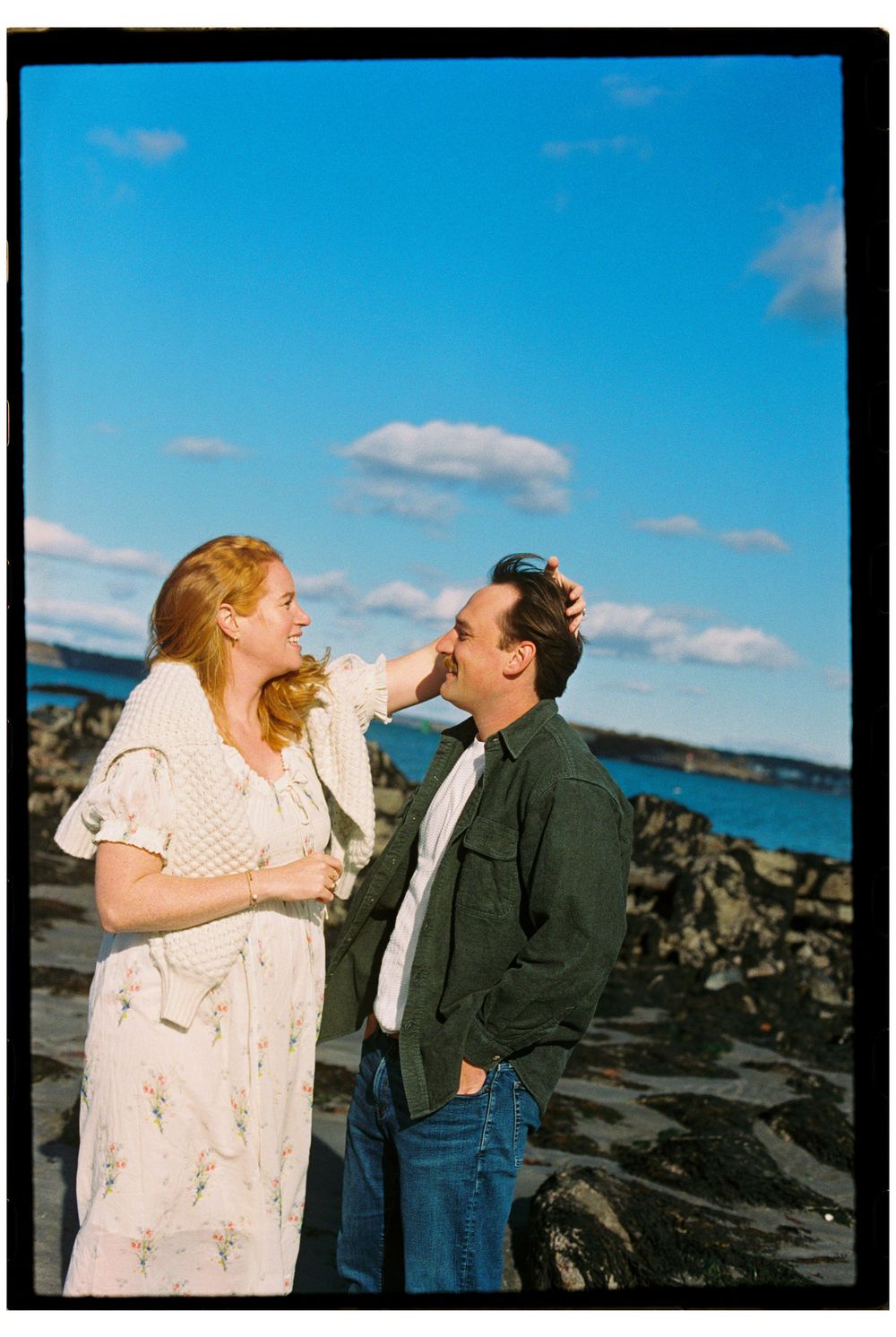 Photograph of couple smiling and laughing together while she fixes his hair during a sunny maternity shoot in South Portland, Maine.