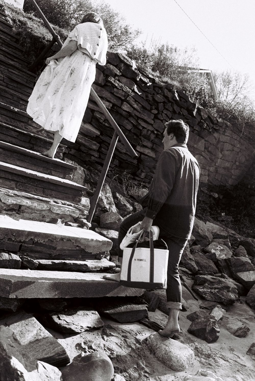 Couple expecting a baby climb the stairs together at the beach on black and white film on a sunny November day in South Portland, Maine.