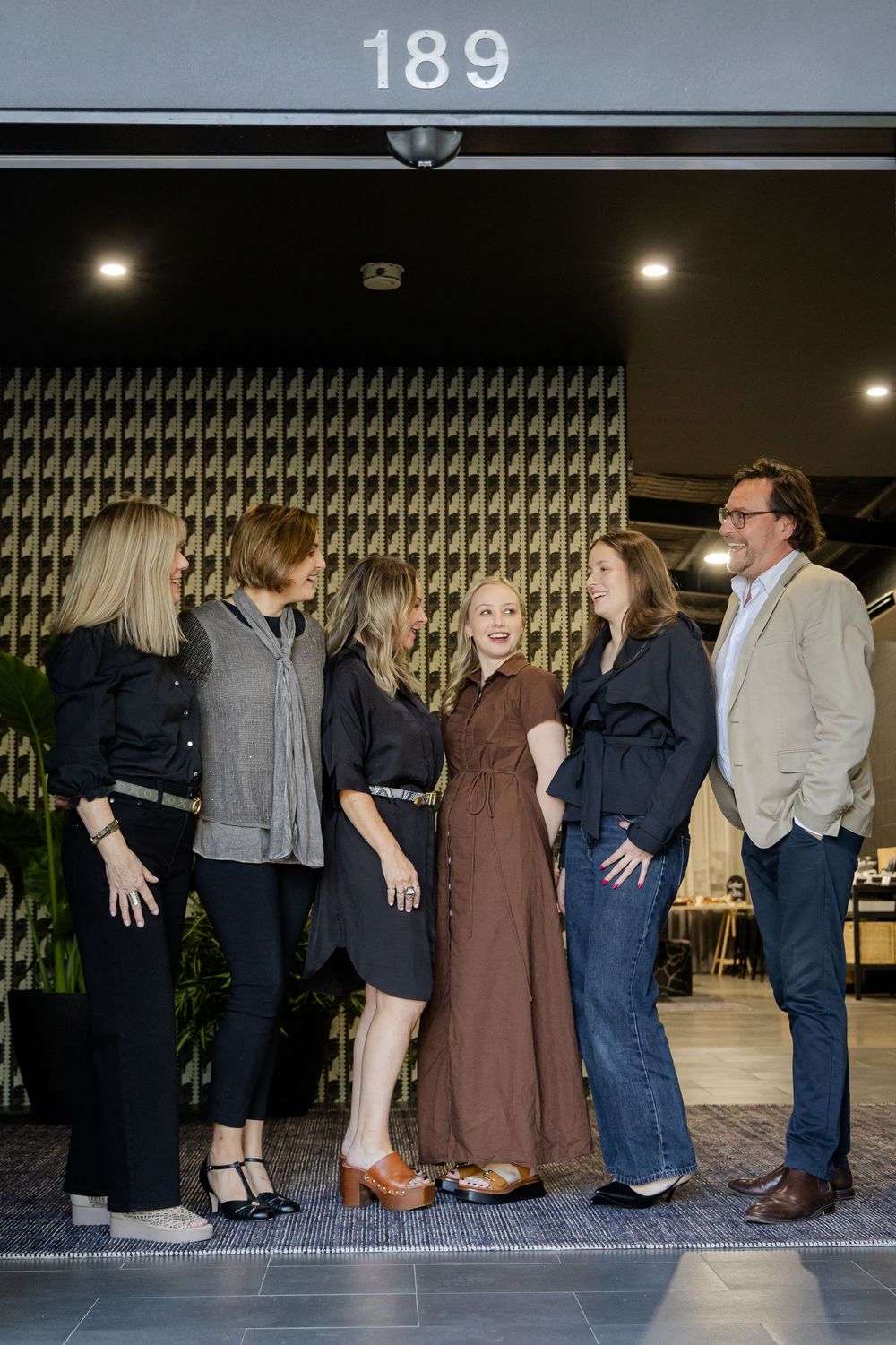 Five professionals pose together outside a modern building entrance marked 189 at an interior design event.