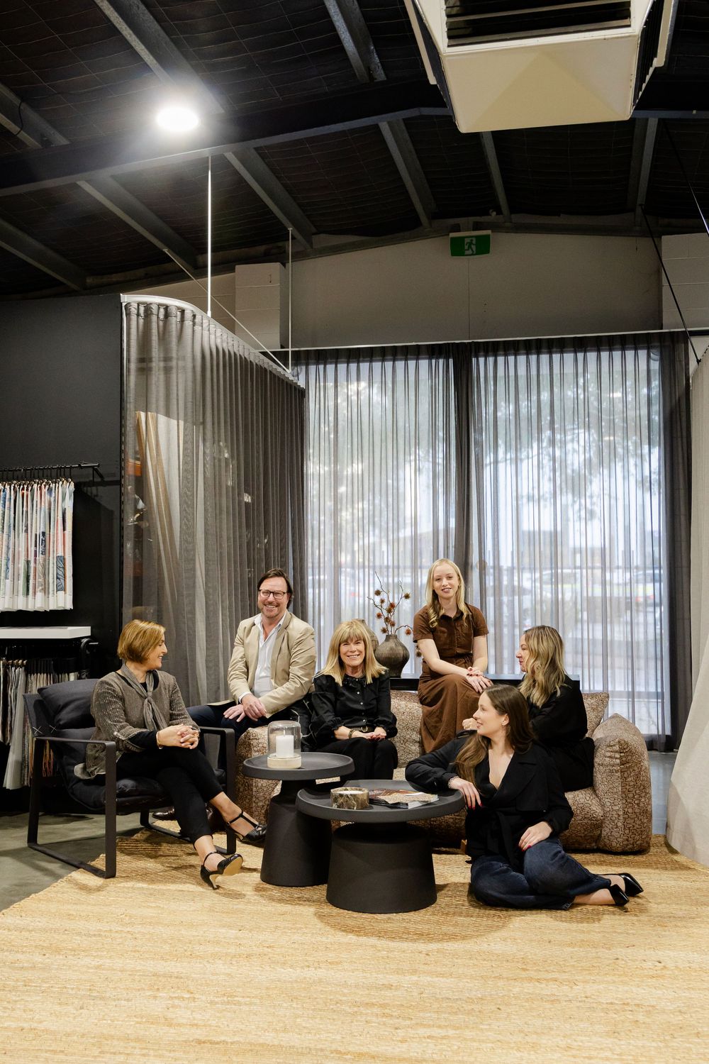 Group of seven professionals socializing in a stylish dark modern showroom with curtains.