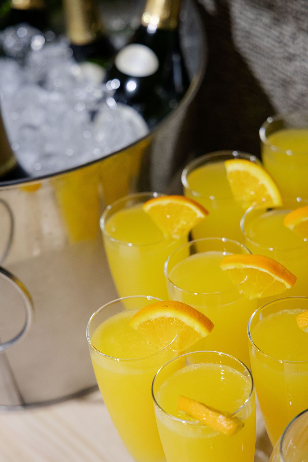 Glasses of fresh orange juice with orange slices beside champagne on ice.