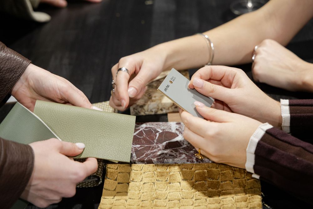 Close-up of hands examining and comparing interior design material swatches including fabric and tile samples.