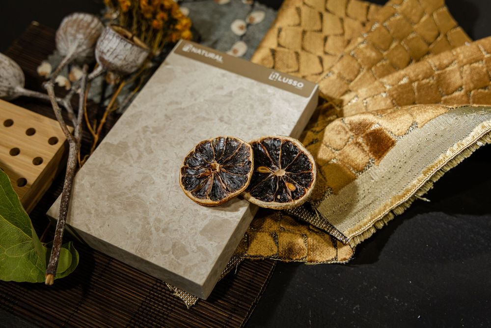Flat lay of marble sample book with dried orange slices, textured gold fabric, and botanicals.