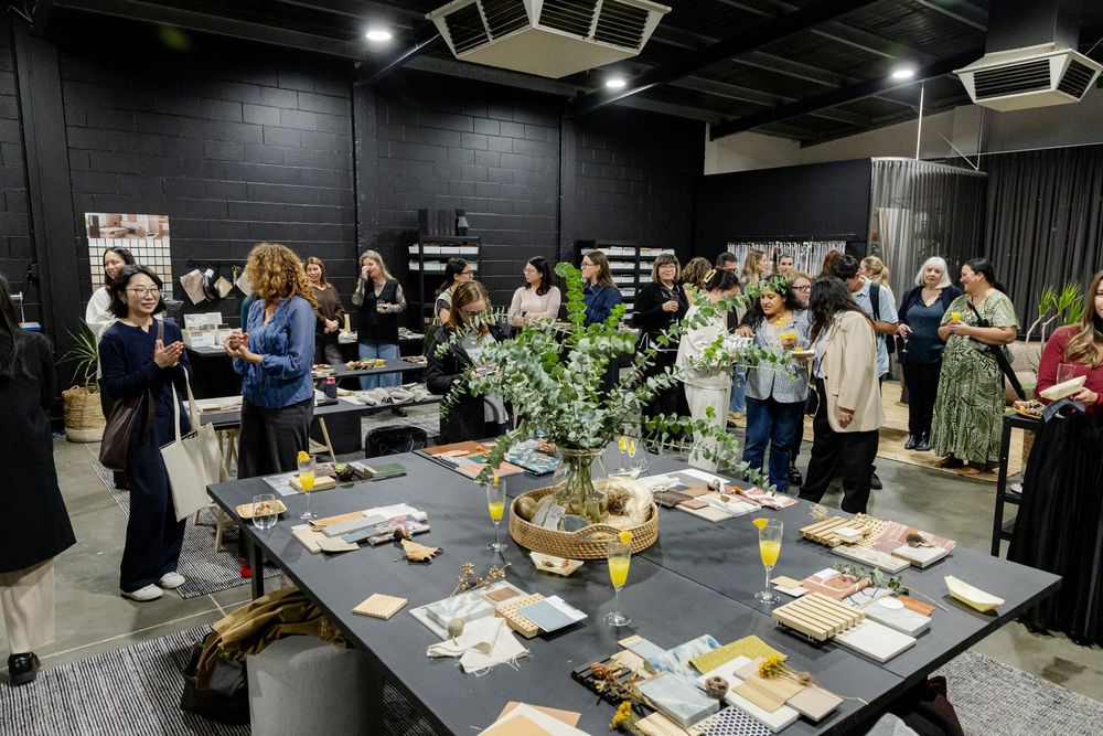 Group of people networking at a design event around a dark table with floral arrangements and printed materials.