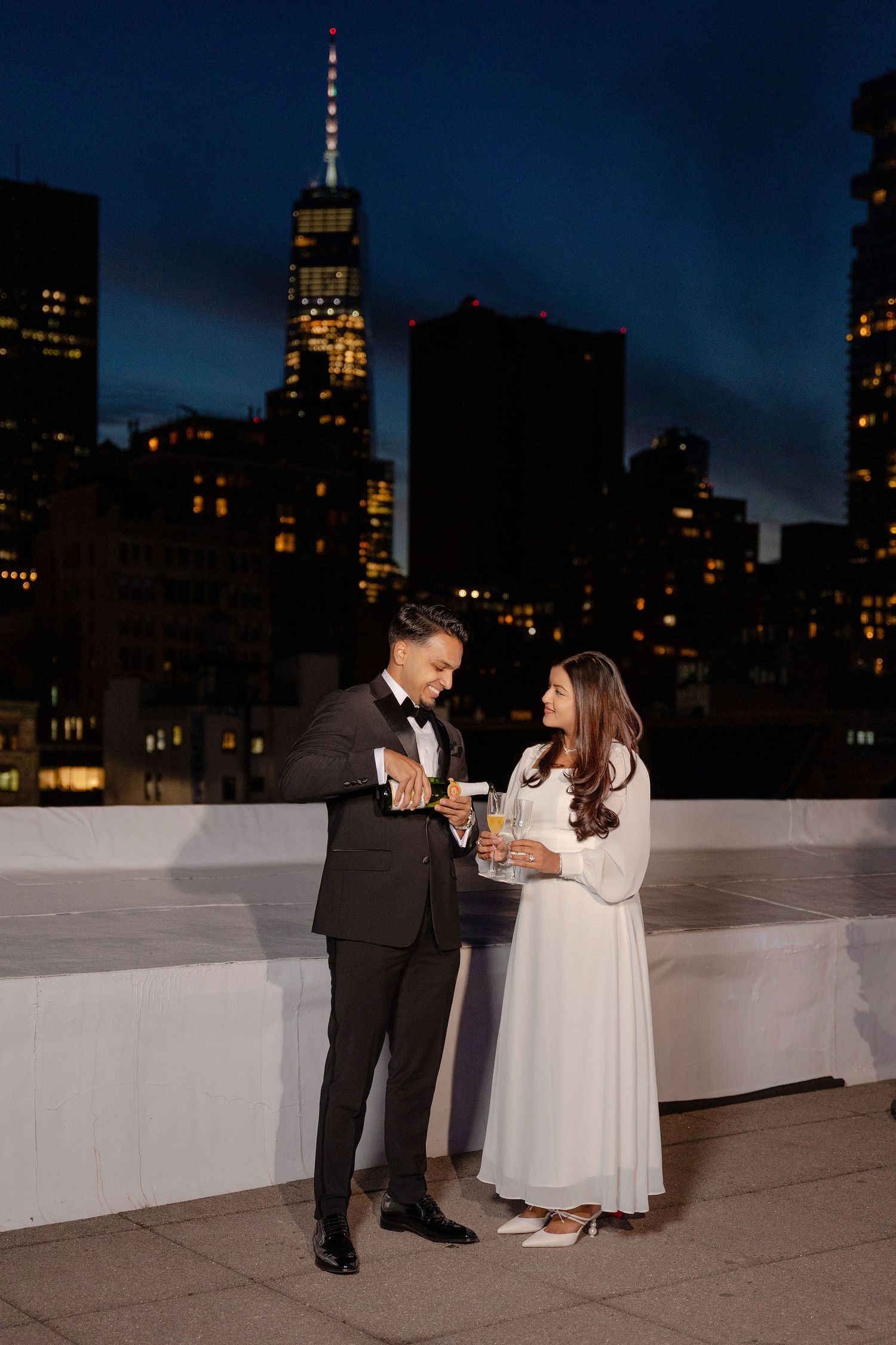 Couple toasting champagne on NYC rooftop at night with illuminated skyline and Empire State Building backdrop.